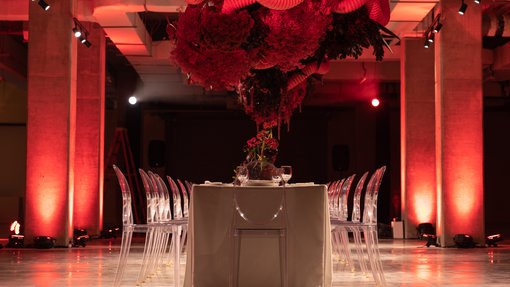 dinner set up in a room with red lights and red flower arrangement from the ceiling