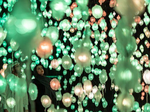 Two people looking at artwork by Pipilotti Rist of hanging lights in green and orange.