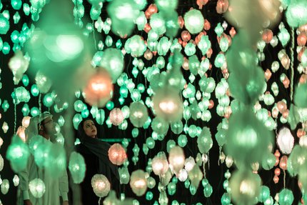 Two people looking at artwork by Pipilotti Rist of hanging lights in green and orange.