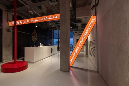 Picture of Al Jazeera reception desk with two hanging light up banners saying "human stories: global perspectives" in arabic and in english