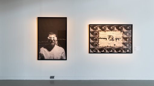 Two black and white artworks in a gallery, one depicts a blindfolded man and the other showcases several eyes.