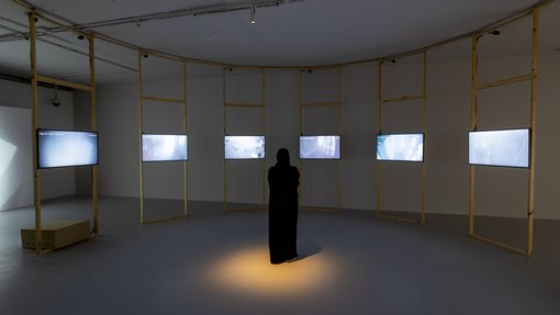 A woman standing in a room surrounded by video screens