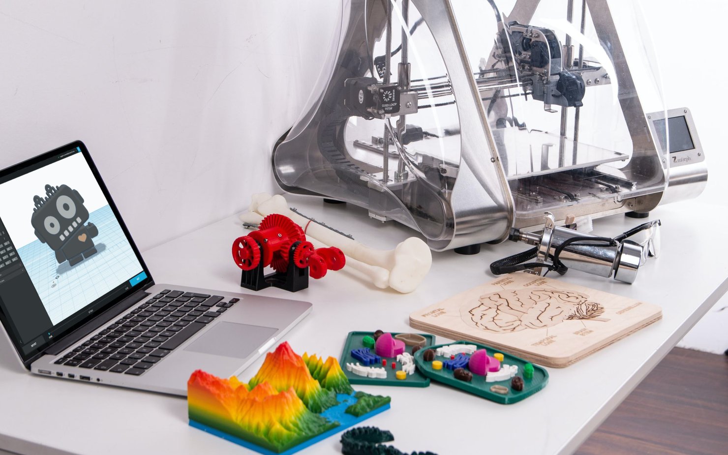 A 3D printer in the background with multi-coloured renders and sketches in the foreground