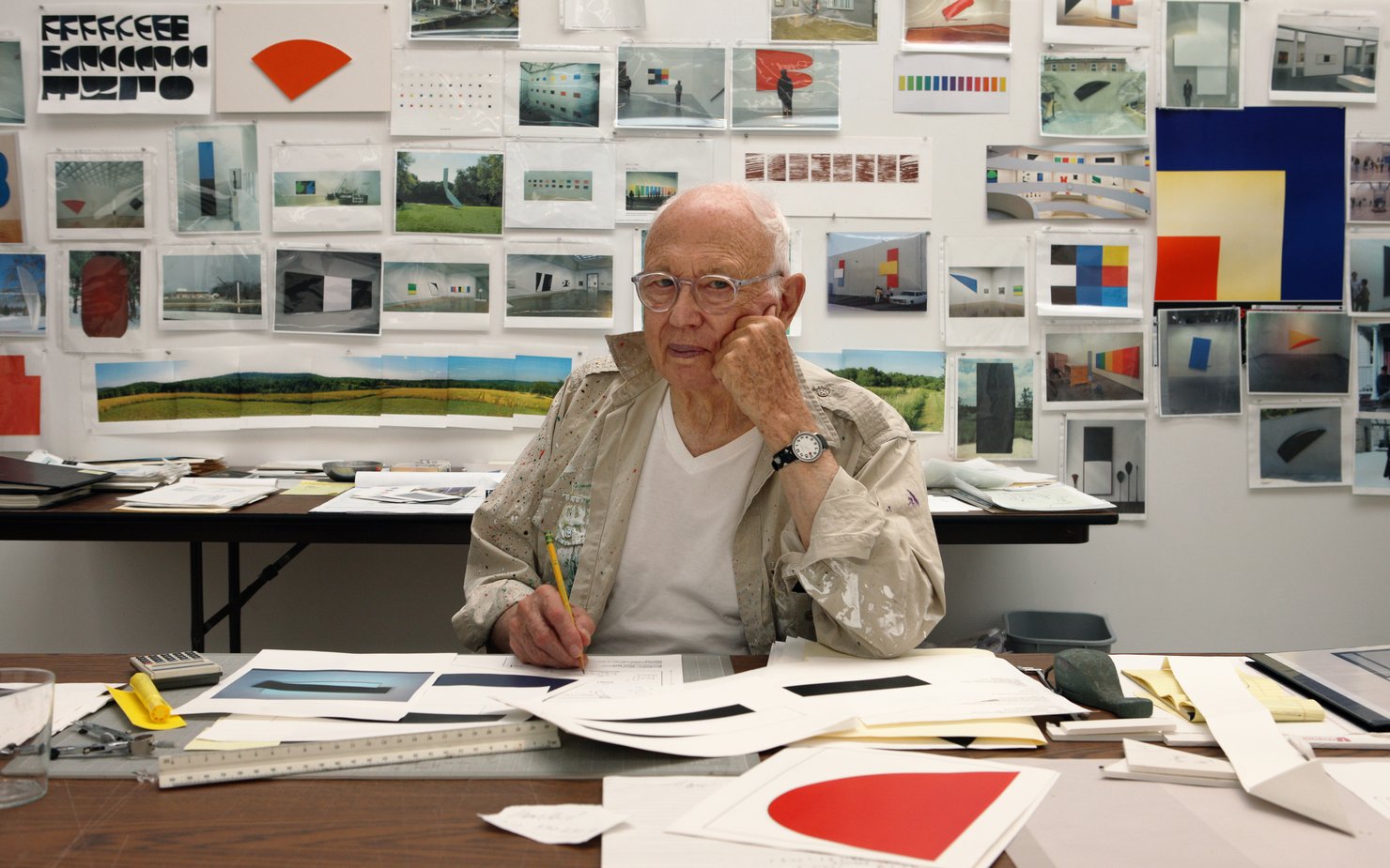 old artists in his studio with paper around him