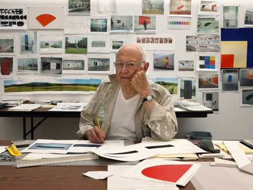 old artists in his studio with paper around him