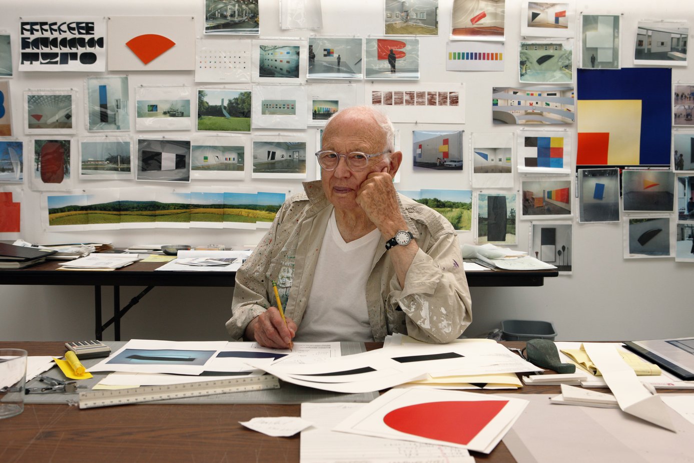 old artists in his studio with paper around him