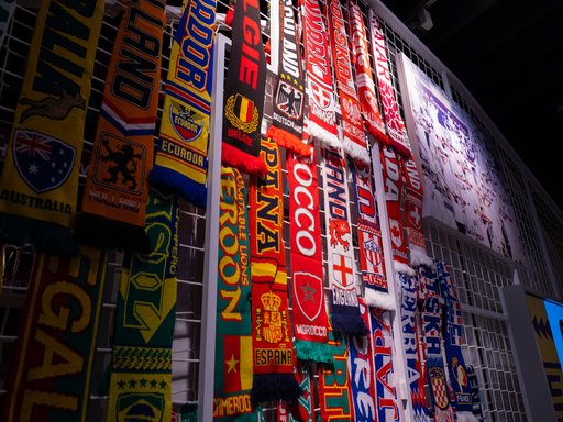Photo of multiple, colourful football scarves hanging on a white, caged, frame.