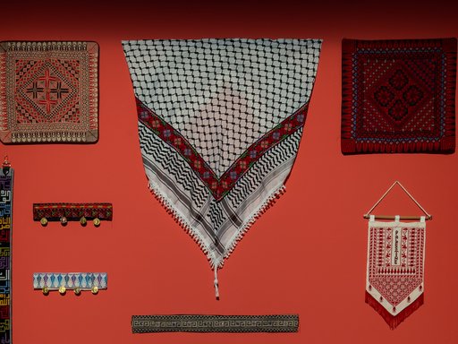 Different embroidered textiles hang against a red wall.