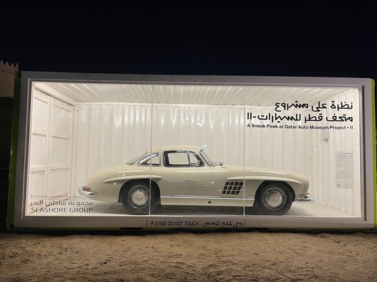 An off-white 1955 Mercedes-Benz 300SL Gullwing car in a display case.