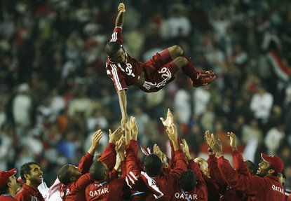 The Qatar football team is shown throwing player number 26 in the air in celebration.