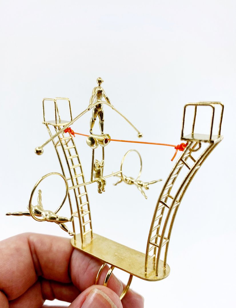 A golden rings with a design of a man balancing on a red tightrope.