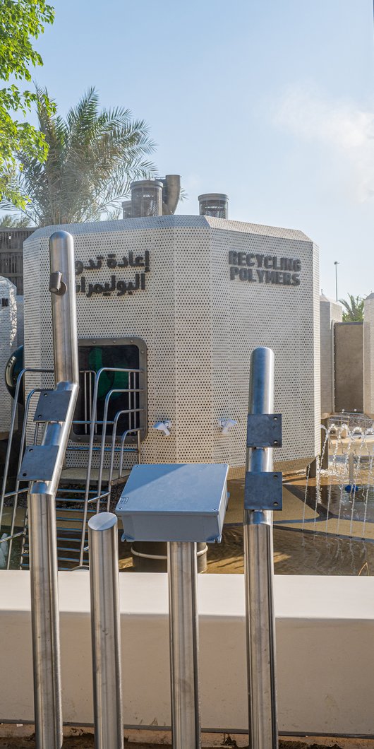Picture of a recycling plant themed playground, at the background is a tower and written on top of it is ''recycling polyesters''