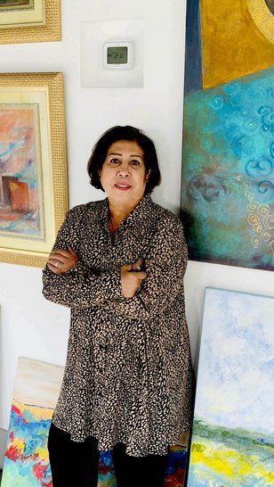Ruwad Artist Wafika Sultan Al-Essa standing next to her paintings in her studio at the Fire Station.