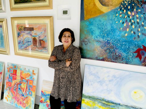 Ruwad Artist Wafika Sultan Al-Essa standing next to her paintings in her studio at the Fire Station.