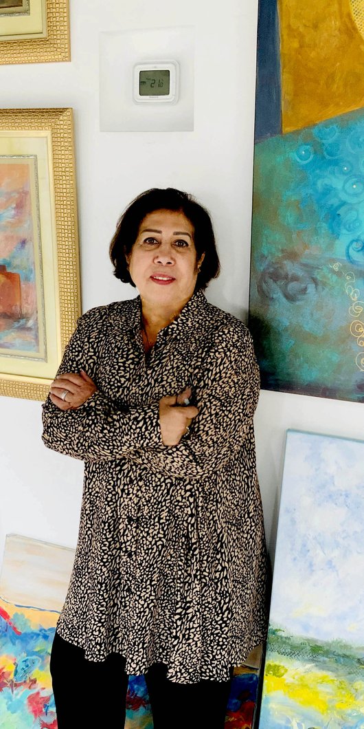 الفنانة الرائدة وفيقة سلطان العيسى تقف بجانب لوحاتها في الاستوديو الخاص بها في مطافئ.
