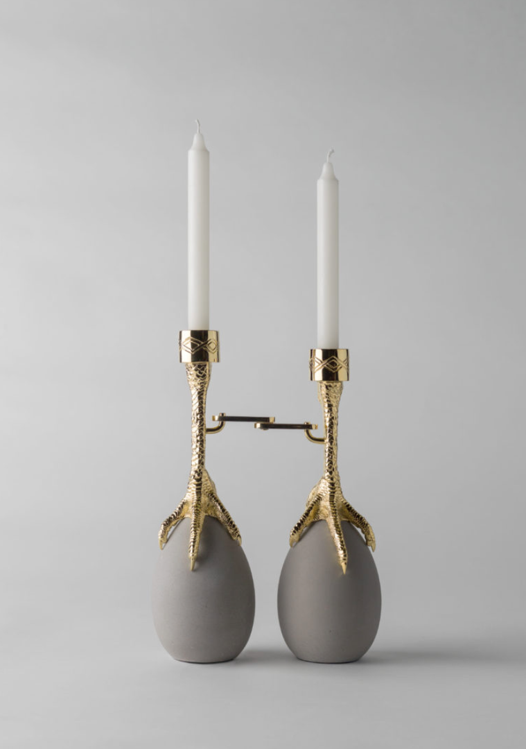 A golden candle holder with a design of two birds feet and two eggs.