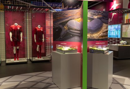 A museum display with maroon football kitted mannequins behind glass and a model of a stadium with the words Education City Stadium visible.
