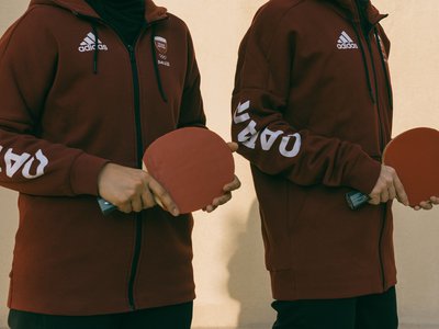 Two people dressed in sports clothes with brand logos and 'Qatar' written on the sleeves, holding ping pong bats.
