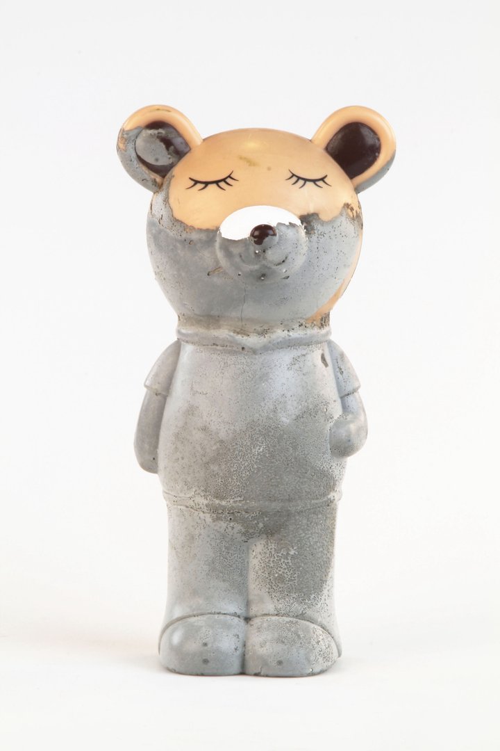 Grey concrete teddy bear figure with a golden head, closed eyes and long eyelashes