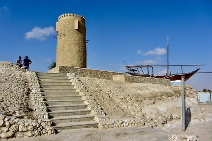 The Al Khor stone tower with two people standing at the top of a flight of steps leading to the tower