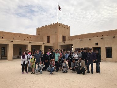 A bunch of visitors pose for a picture with the Al Zubara Fort right behind them
