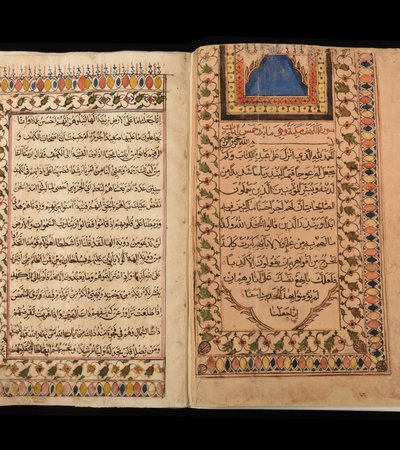 Photo of the Al Zubarah Qur'an opened to reveal the Al Kahf chapter of the Holy Qur'an in Arabic script, surrounded by intricate designs and colours.