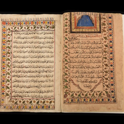 Photo of the Al Zubarah Qur'an opened to reveal the Al Kahf chapter of the Holy Qur'an in Arabic script, surrounded by intricate designs and colours.