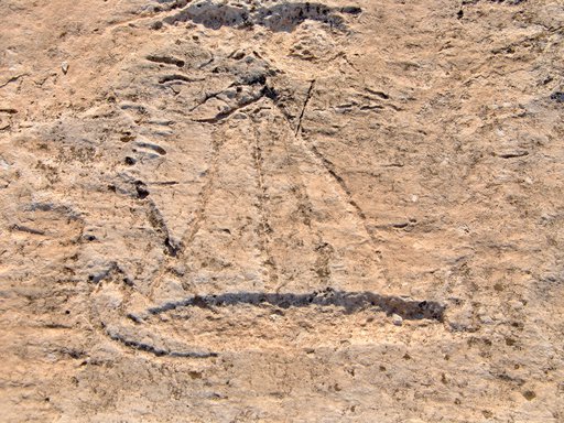 A sand coloured rock face with the outline of a boat with a sail carved into its surface