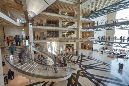 Atrium space with curved staircases at the Museum of Islamic Art, busy with museum visitors