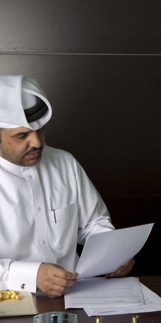 Two men in traditional Qatari attire study a document
