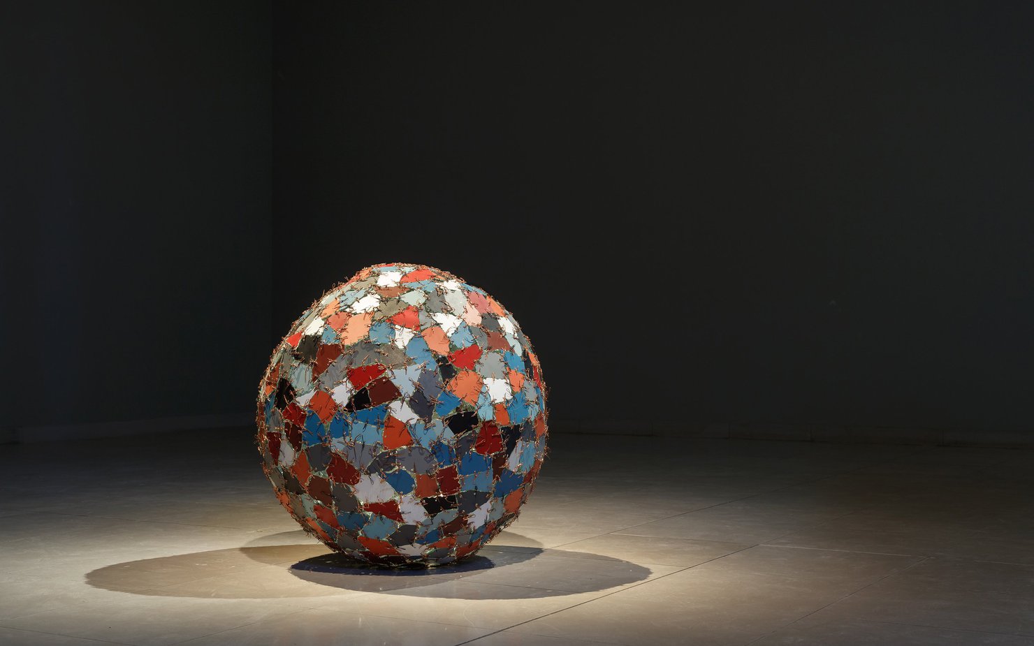 A spotlight on the object Chaos+Repair=Universe showcasing a sculpture with coloured mirror fragments stitched into a ball shape with metal wires
