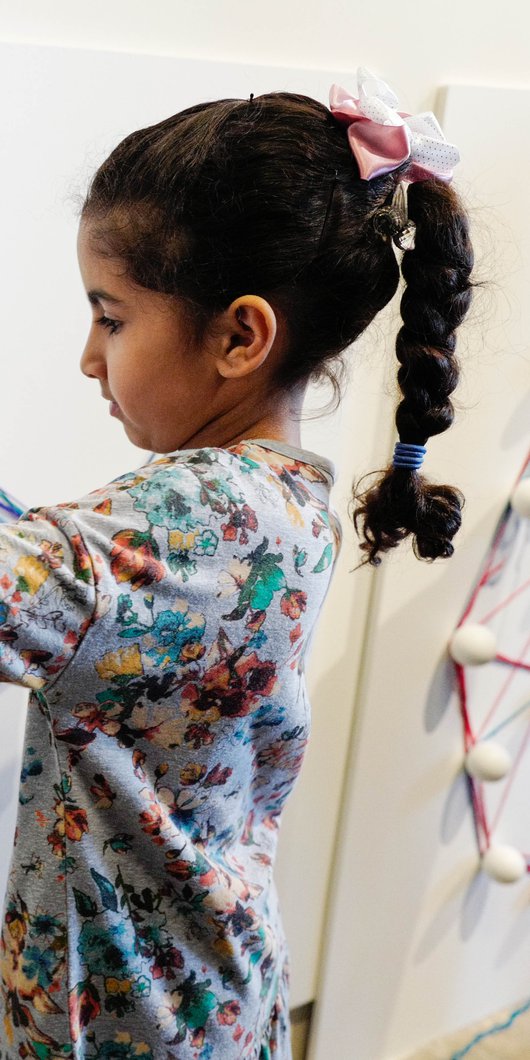 طفلة صغيرة تصنع أشكالاً هندسية على جدار باستخدام خيط، في دد، متحف الأطفال في قطر