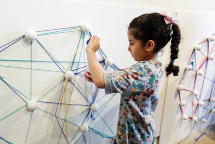 A young child making geometric shapes on a wall with string, at Dadu, Children's Museum
