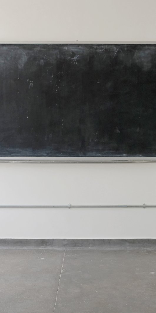 An empty white room with a blackboard on the wall and a pile of wooden stools.