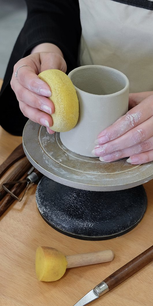Close view of a woman making a pot in clay on a pottery wheel.