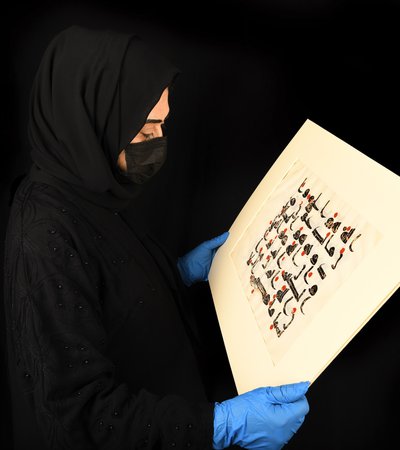 Woman in abaya holding out a historic Arabic manuscript in landscape position