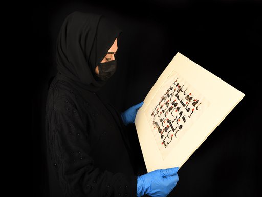 Woman in abaya holding out a historic Arabic manuscript in landscape position