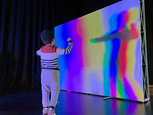 صبي يقف أمام شاشة بيضاء تعكس ظله بألوان مختلفة