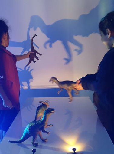 Children experimenting with light to create shadows of their toy dinosaurs