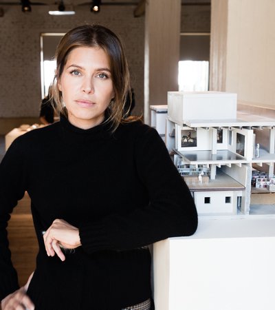 Portrait of Dasha Zhukova leaning against a table featuring an architectural model