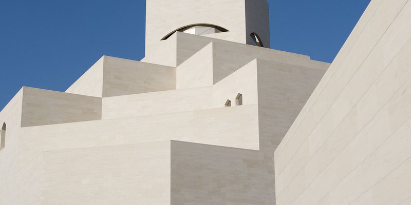 Detail of the white angular exterior of the Museum of Islamic Art with a blue cloudless sky in background