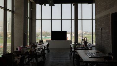 Education Studio at Fire Station with tables, a TV screen and panoramic windows with a view of Al-Bidda park.