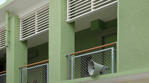 A green coloured mid-century building with balcony and close-up of a megaphone.