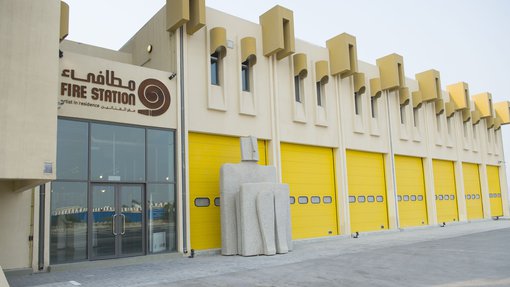 Exterior of The Fire Station Artist in Residence building showing its bright yellow shutter doors and sculpture at the entrance