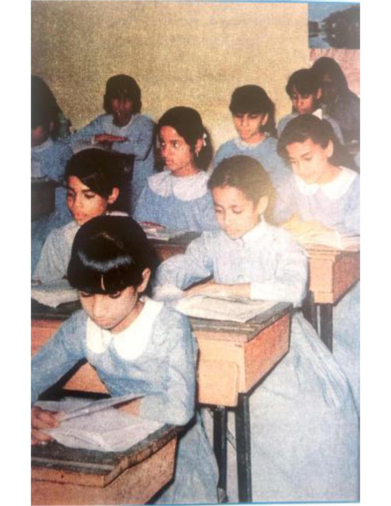 Old picture of elementary female students sitting on individual desks writing.