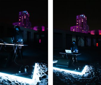 An Arab woman stands at a mixing desk with a laptop, outside at night time.