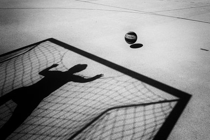 A photo of a person's shadow as they stand in goal with a ball bouncing towards them.
