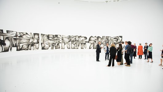 مجموعة من الزوار في الرواق جاليري وتظهر في الخلفية أعمال من معرض الفنان ضياء العزاوي