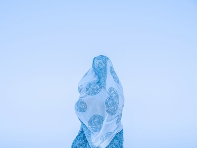 A photo of a female with white and blue fabric wrapped around them standing against a light blue background.