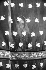 A black and white photo of a woman standing behind a length of patterned fabric.